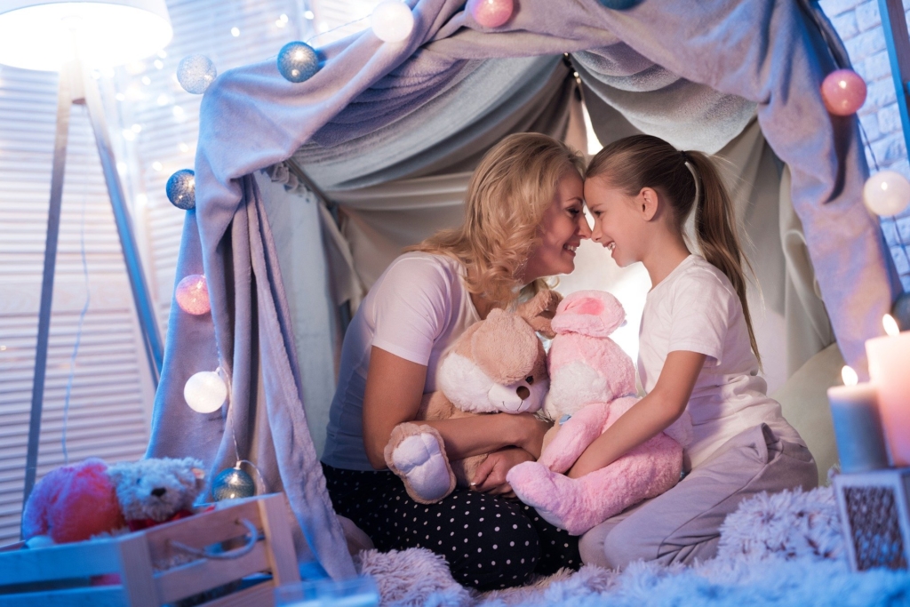 Quarantine lifestyle mom and daughter under blanket fort camping inside